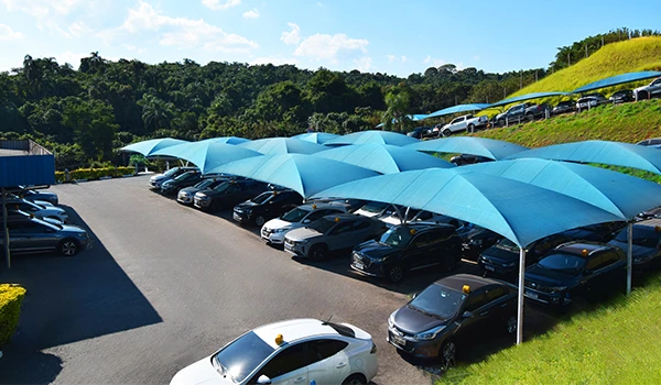 Imagem do estacionamento em Guarulhos Airport Park, com vários carros sob coberturas azuis, rodeado pela natureza. Um local ideal para estacionar com proteção contra o sol. 