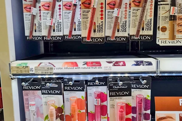 Exibição de produtos de maquiagem Revlon em uma prateleira, incluindo batons e produtos labiais. Variedade de cores e texturas disponíveis para todos os gostos.