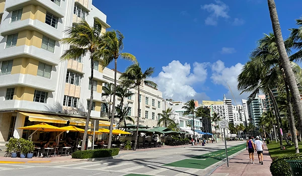 Imagem de um trecho da Ocean Drive em Miami com palm trees, calçadão e edifícios art déco. Atrações de South Beach.