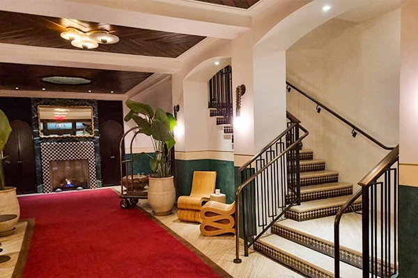 Hall de entrada do Esmé Hotel com escadas e decoração elegante, destacando tapete vermelho e detalhes arquitetônicos sofisticados.