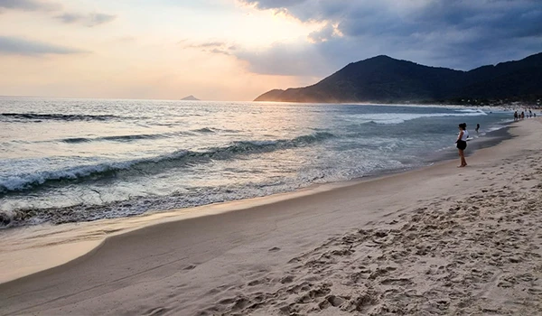 Imagem do final de tarde na praia de Maresias, com uma pessoa observando o pôr do sol dourado.