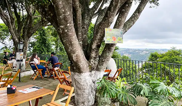 Bar do Cristo com vista de um café ao ar livre em uma área arborizada, com mesas de madeira e clientes desfrutando do ambiente relaxante e da natureza, dica para ir depois da visita em Serra Negra da Fontana di Trevi.