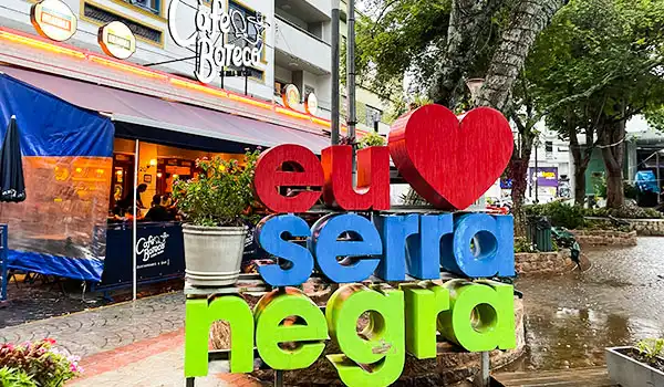 Placa colorida com a frase 'Eu ♥ Serra Negra', destacando a cidade em um ambiente urbano atraente, ideal para turismo e lazer, bem próximo da Fontana di Trevi.