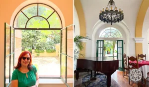 Deusa Rodrigues junto a uma janela aberta, com vista para um jardim verde. Ao fundo, um ambiente interno elegante com piano e decoração sofisticada.