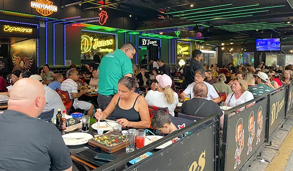 Vista do interior do restaurante D'Jones, com mesas lotadas, pessoas comendo e um ambiente animado, ideal para refeições em família e amigos. Em Serra Negra depois de visitar a Fontana di Trevi é uma opção para almoçar.