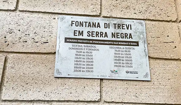 Placa informativa sobre os horários de funcionamento Serra Negra Fontana di Trevi incluindo detalhes para diferentes dias da semana.