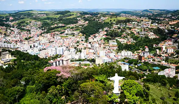 Vista aérea de Teresópolis, cidade no estado do Rio de Janeiro, cercada por áreas verdes, com o Cristo Redentor ao fundo e a cidade no centro, mostrando uma paisagem urbana com colinas e florestas.