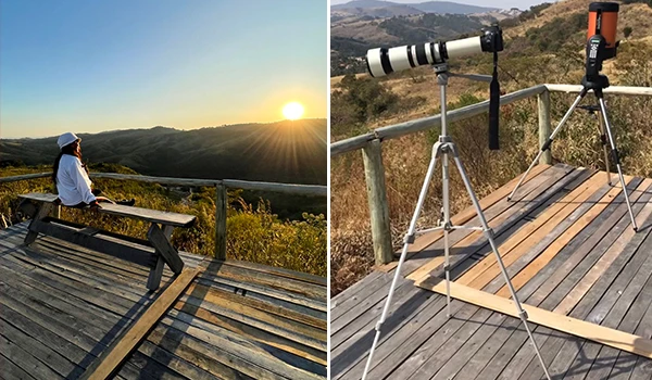 Ponto de vista de uma pessoa observando o pôr do sol com um telescópio montado em um tripé, em uma paisagem natural.