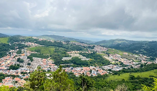 Vista panorâmica de uma cidade rodeada por colinas e vegetação, mostrando a arquitetura urbana e o cenário natural ao redor.