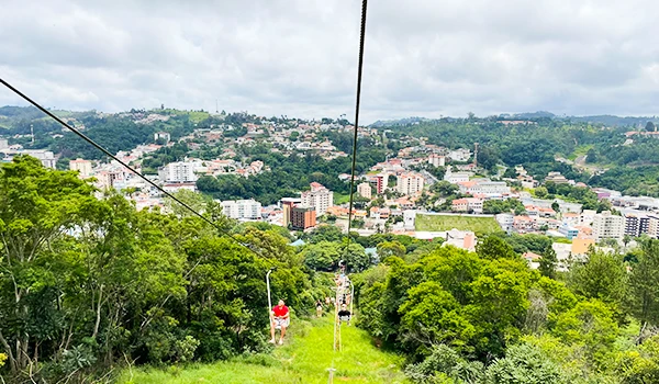 Foto do teleférico Serra Negra, com visitantes nas cadeirinhas e vista panorâmica de uma cidade ao fundo, com montanhas e vegetação ao redor, além da Fontana di Trevi também é bem visitado.