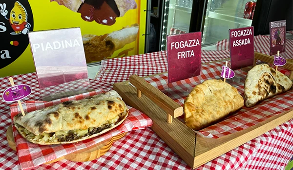 Imagem de pratos típicos italianos com piadina e fogazza farta sobre toalha quadriculada vermelha e branca, destacando a culinária.