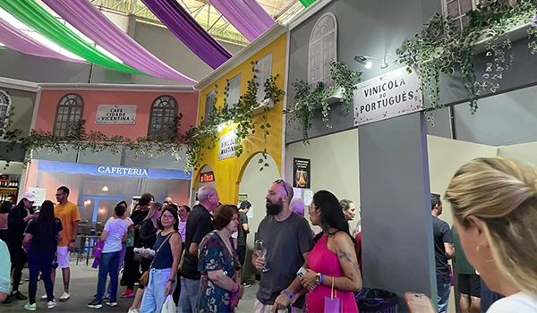 Pessoas mingling em um evento de vinhos, com decoração vibrante e estandes de vinícolas, incluindo a 'Vinícola Portuguesa' na típica Festa da Uva de Jundiaí.