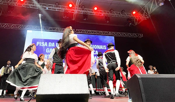 Apresentação de dança tradicional brasileira no evento Pisa da Luz, mostrando dançarinos com trajes típicos em um palco iluminado.