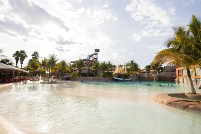 Imagem de um parque aquático com piscina e tobogãs, rodeado por palmeiras e céu azul. Ente os Hotéis e Parques para o Carnaval é um ambiente ideal para diversão e relaxamento em família.