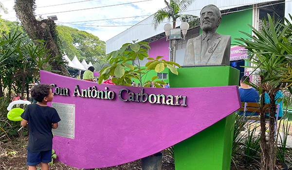 Estátua de Tom Antônio Carbonari em um espaço verde, rodeada por plantas, com crianças na ípica Festa da Uva de Jundiaí.