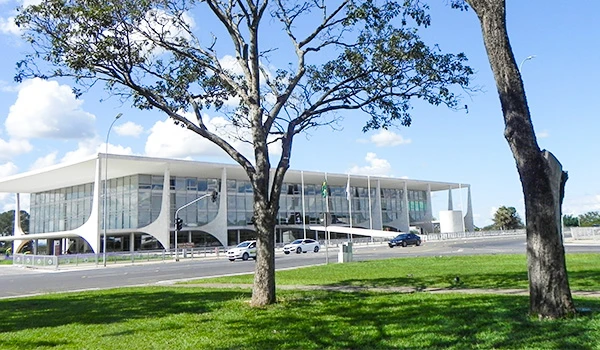 Fachada do Palácio do Planalto, com design moderno e elegante, rodeado por árvores e céu azul.