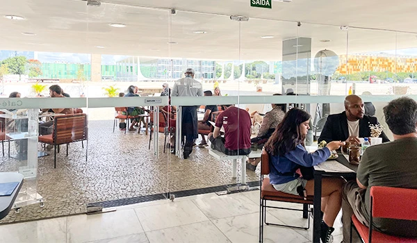Imagem de um restaurante moderno com várias mesas e pessoas consumindo refeições em um ambiente iluminado e aconchegante.
