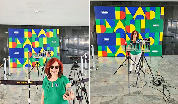 Deusa Rodrigues em frente a um fundo colorido, pronta para coletiva de imprensa, com microfones e câmeras ao redor.