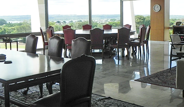 Ambiente moderno de escritório do Presidente da República com mesa grande e cadeiras ao redor, vista panorâmica para a natureza, ideal para reuniões e trabalho em equipe.