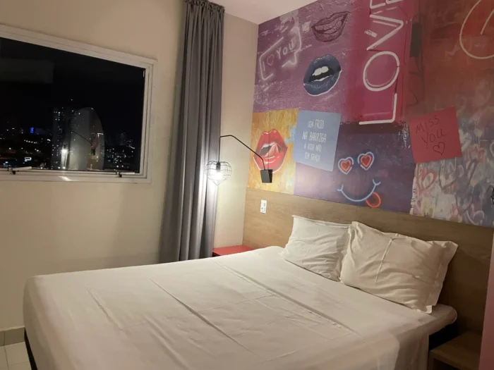 Quarto moderno e acolhedor com decoração vibrante, fachada de grafite nas paredes e vista noturna da cidade. Dicas sobre o que fazer em Franca.