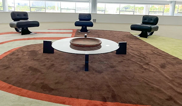 Sala moderna com poltronas pretas e mesa de vidro sobre um tapete marron, ideal para decoração contemporânea e estética minimalista.
