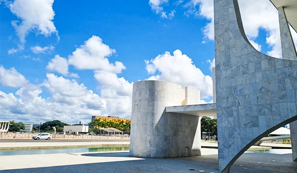 Vista da arquitetura moderna com céu azul e nuvens, destacando a estrutura de concreto ao lado espelho d´água no Palácio do Planalto em Brasília.
