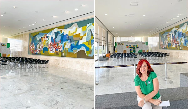Imagem de um espaço interno com arte moderna na parede, cadeiras dispostas e Deusa Rodrigues sentada em uma área destinada a jornalistas. Dicas sobre a visita ao Palácio do Planalto.