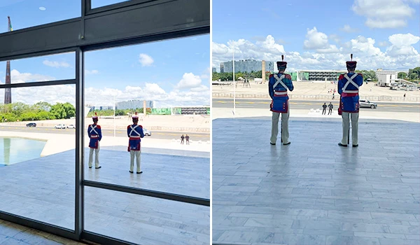 Guarda do Palácio do Planalto em Brasília, na área externa com vista para o horizonte claro e ensolarado. A imagem mostra dois guardas em posição de atenção em um espaço amplo e moderno.