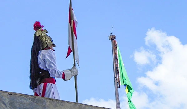 Imagem do Guarda de Honra do Palácio do Planalto o com armadura antiga segurando uma bandeira, em um evento patriótico com céu azul ao fundo.