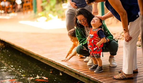 Família se divertindo em contato com a natureza, observando peixes em um lago de um restaurante de SP. Um dos presentes para o Dia das Mães com gastronomia.