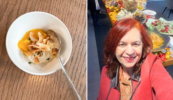 Imagem de uma sobremesa tailandesa em uma tigela branca ao lado de uma mulher sorridente com cabelos castanhos e cabelo cacheado, em ambiente de feira ou evento com flores ao fundo.