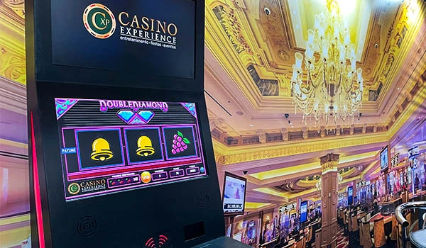 Máquina de caça-níquel Double Diamond em um cassino com decoração luxuosa, teto com iluminação dourada e colunas imponentes, ambiente elegante e vibrante. Evento Casar.com para Noivas.