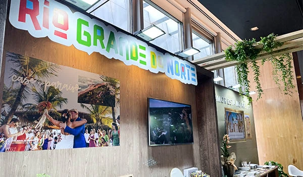 Ambiente decorado com banners de evento na Rio Grande do Norte, com público apreciando uma apresentação ao ar livre, decorações naturais e ambiente acolhedor. Evento Casar.com para Noivas.