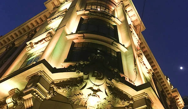 Edifício histórico iluminado à noite com detalhes arquitetônicos impressionantes e a lua ao fundo, destacando a beleza urbana. Festival do Café em São Paulo.