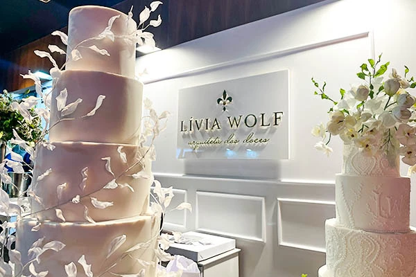 Bolos de casamento decorados com flores brancas e detalhes elegantes em um evento de casamento com o nome 'Lívia Wolf'.
