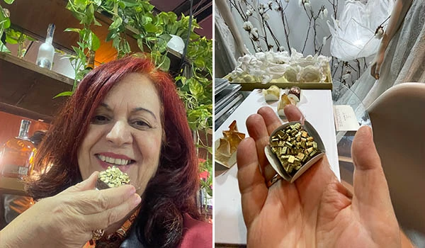 Deusa Rodrigues recebendo um doce de presente em forma de joia dourada em uma loja, com ambiente decorado e plantas ao fundo.