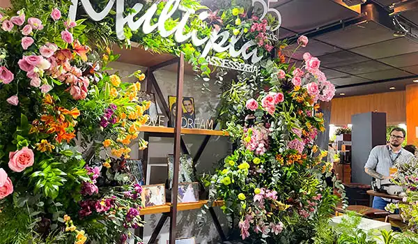 Decoração de ocasião especial com flores coloridas em um evento no interior de um espaço com ambientes modernos e pessoas ao fundo. Evento Casar para Noivas.