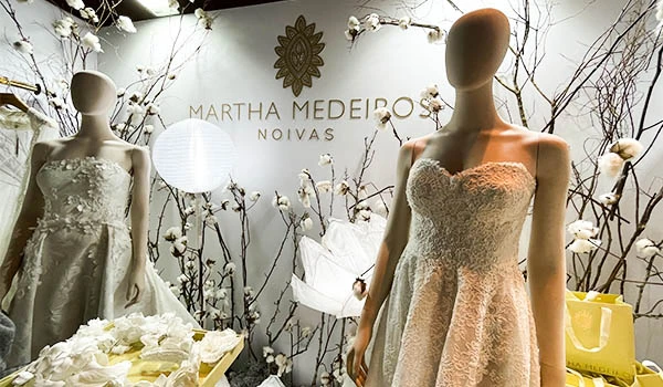 Vitrine de casamento com manequins vestidos de noiva, decoração de flores brancas, e inscrição 'Martha Medeiro Noivas' ao fundo em loja especializada em vestidos de noiva e acessórios. Evento Casar para Noivas.