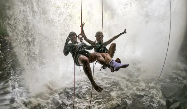 Duas pessoas praticando tirolesa sobre uma cachoeira, demonstrando aventura e espírito de exploração na natureza exuberante.