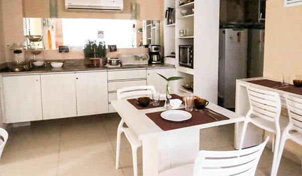 Imagem de uma cozinha moderna decorada em estilo clean com móvel embutido, mesa de jantar branca com cadeiras de madeira, utensílios e eletrodomésticos, iluminada de forma suave, criando um ambiente aconchegante e funcional.