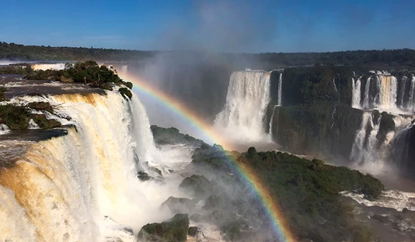 Cataratas do Iguaçu com arco-íris ao fundo, destaque para a grandiosidade da cachoeira e a beleza natural do parque nacional brasileiro.