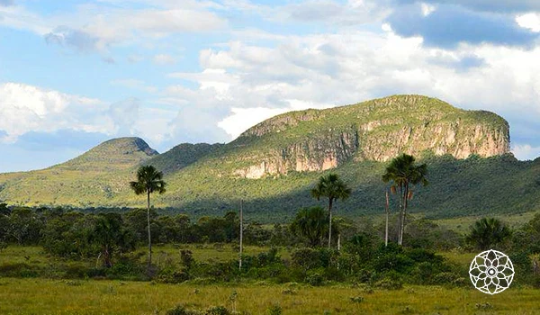 Paisagem natural com montanhas verdes, árvores e céu com nuvens em uma área de mata em uma região de relevo elevado no Brasil.