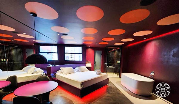 Quarto de hotel moderno com iluminação ambiente, cama de casal, banheira de hidromassagem, decoração com cores vibrantes e fachada moderna, ideal para relaxar.