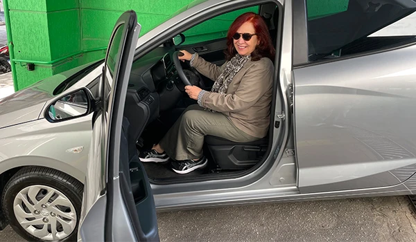 Deusa Rodrigues dirigindo um carro prata, exibindo alegria e confiança ao volante