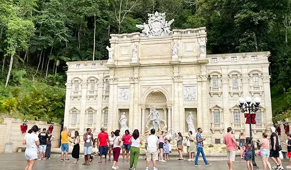 Vista do monumento histórico, com várias pessoas admirando a arquitetura detalhada em um ambiente natural exuberante. Férias na Montanha ou na Praia?