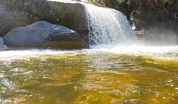 Cachoeira de água cristalina e correnteza no rio, cenário natural com pedras ao fundo, perfeito para ecoturismo e turismo de aventura. Lugares com cachoeira no Brasil.