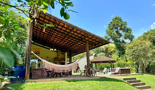 Imagem de uma aconchegante varanda de madeira ao ar livre, rodeada por árvores verdes e céu azul, ideal para momentos de descanso e lazer ao ar livre.