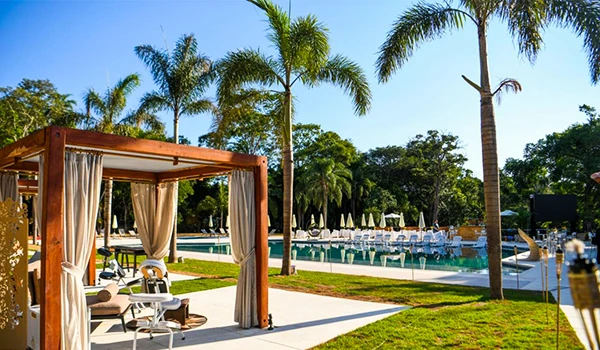 Piscina de resort com espreguiçadeiras, área de descanso e muitas palmeiras ao redor, ideal para relaxamento e lazer ao ar livre.