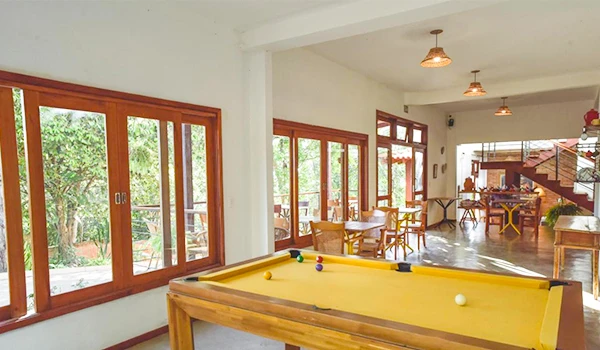 Imagem de uma sala de jogos ensolarada com mesa de sinuca e vista para o jardim, ideal para diversão e lazer em família ou com amigos.