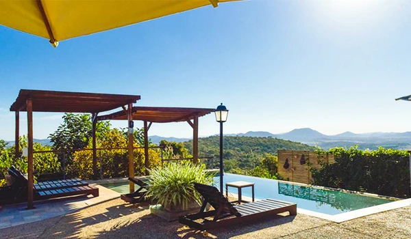 Cena de uma área de lazer ao ar livre com espreguiçadeiras, piscina e vista panorâmica de natureza e montanhas ao entardecer, ideal para relaxar.